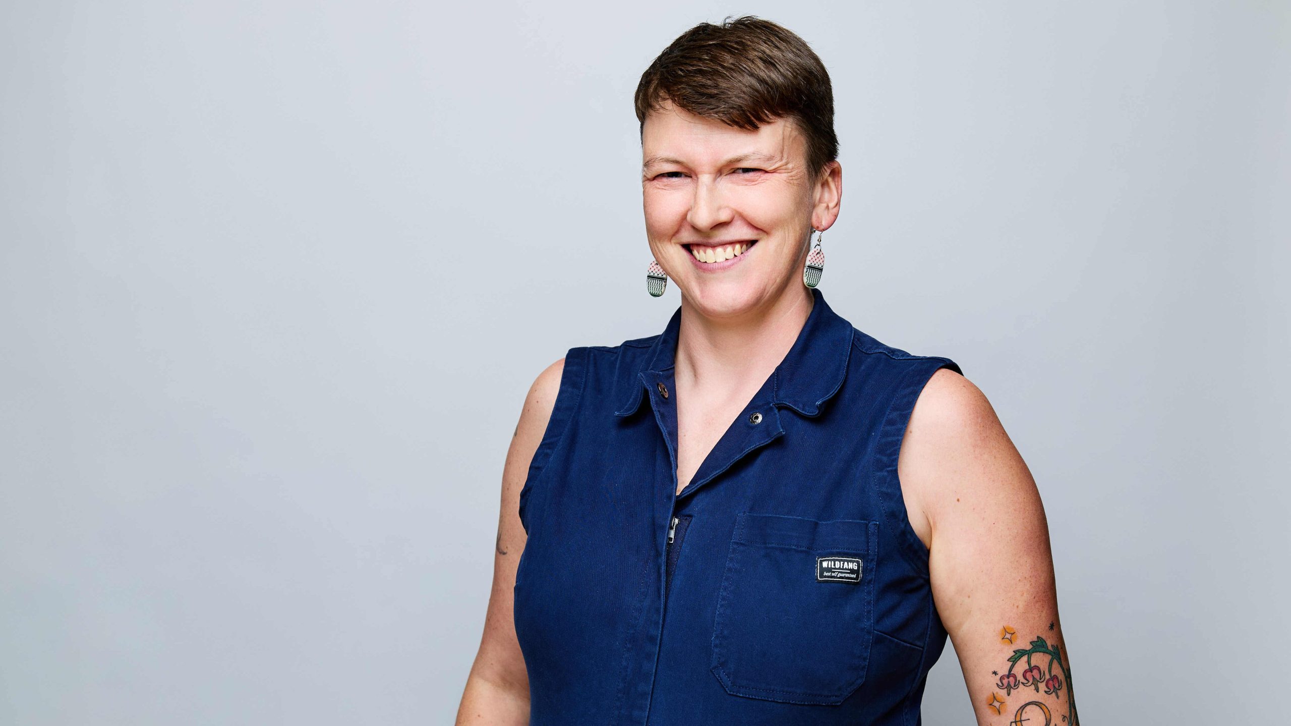 headshot of a white person with short brown hair wearing a dark blue sleeveless jumper and smiling.
